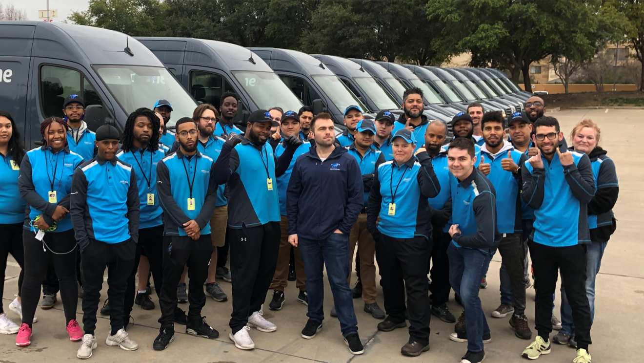 Employees at Patriot DSP stand as a group in front of a fleet of Prime delivery vans.