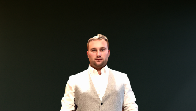 Foto di Simone Pavan. Indossa un completo grigio con gilet. Alle sue spalle il logo Habitat Nest su un fondo nero.