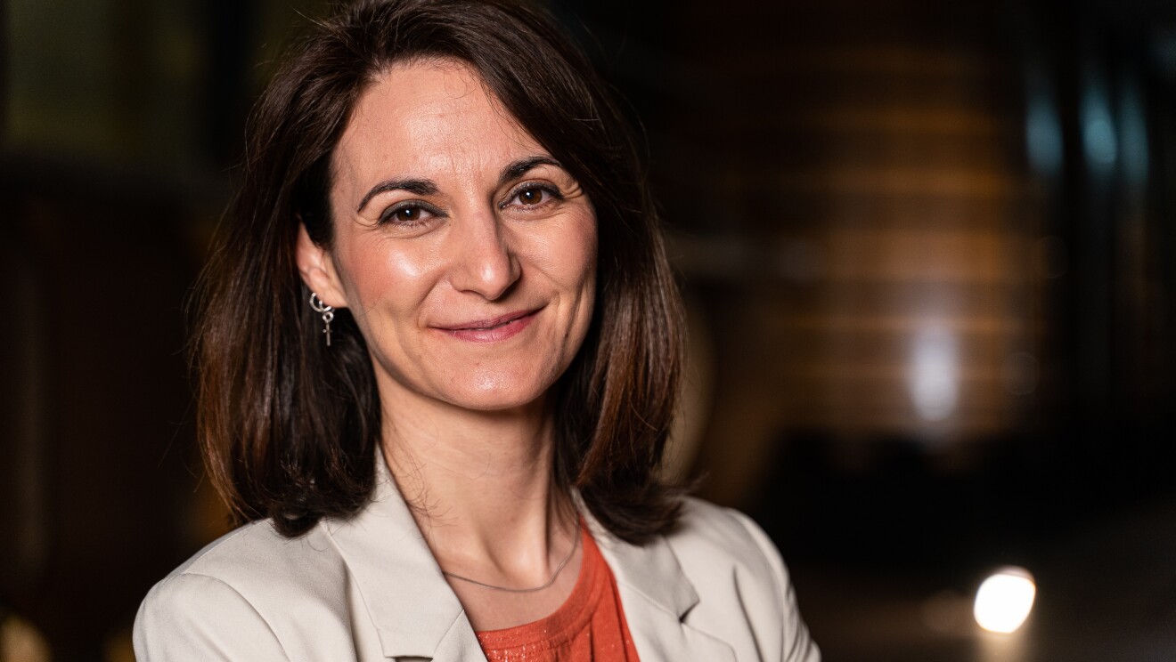 Pilar Moretón, responsable de I+D+I e de Pradorey. Con las tinadas desenfocadas de fondo, aparece ne primer plano y sonriendo Pilar. Media melena castaña con un collar y unos pendientes, una americana blanca y un jersey de color naranja.
