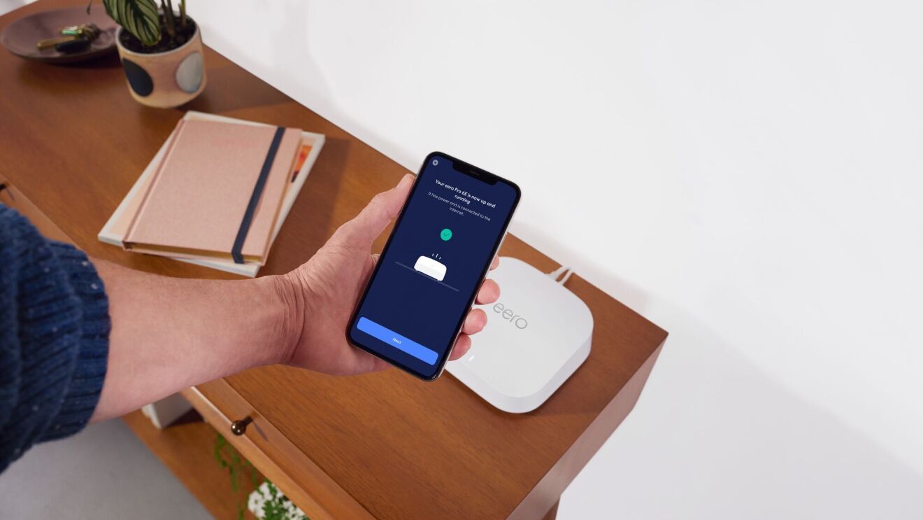 Mano con un teléfono activando el contactless Wi-Fi con el teléfono móvil y un dispositivo eero 