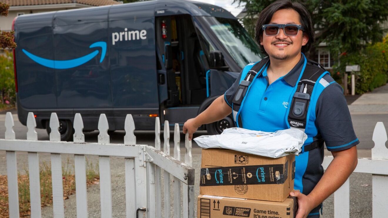 Smiling Amazon delivery driver wearing high-tech smart glasses while holding packages to deliver to a customer.