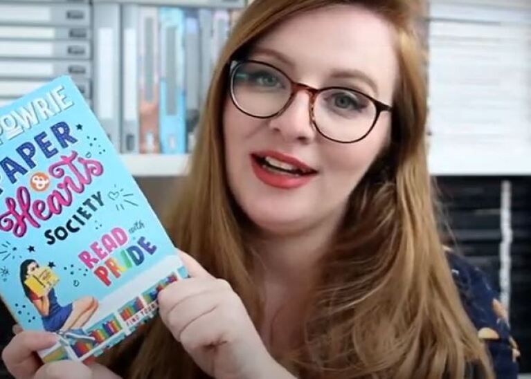 Girl holding a book up and smiling at camera 