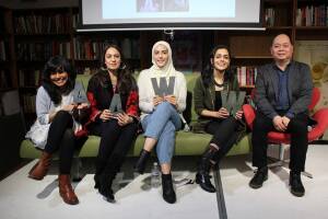 Four women sit on a sofa, holding letters "AAWW," at an Asian American Writer's Workshop. To the right, a male is also shown.  