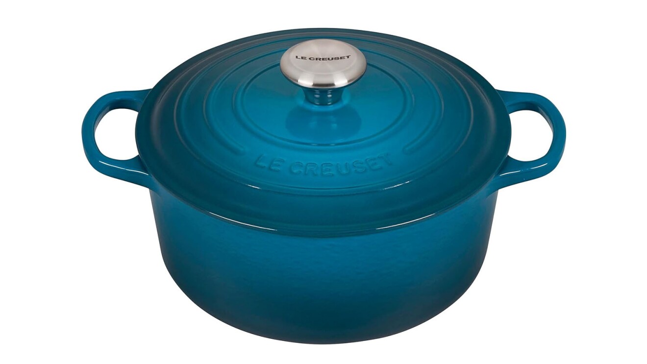 An image of a dark blue dutch oven from Le Creuset. It has a circular pot at the bottom, handles on either side, and a lid with a round, silver handle.