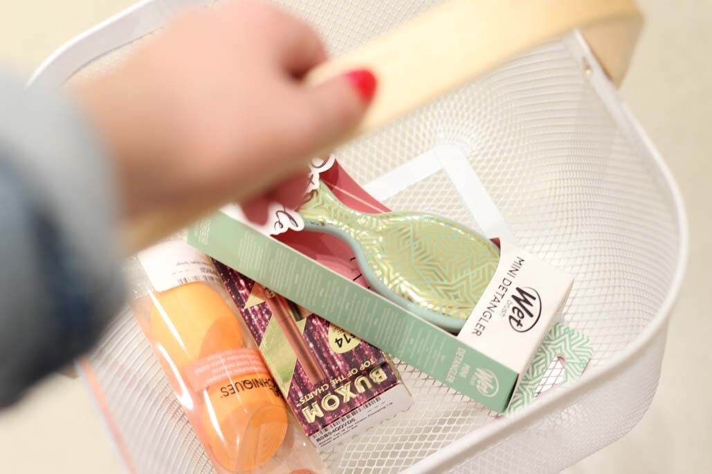 An image of a hand holding a small shopping basket. Inside the basket are several beauty and skincare items.