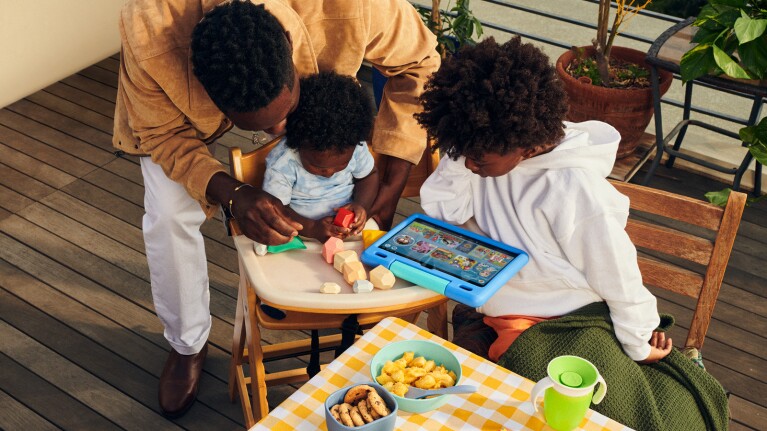 An image of a dad and two kids playing with toys and an Amazon tablet. 