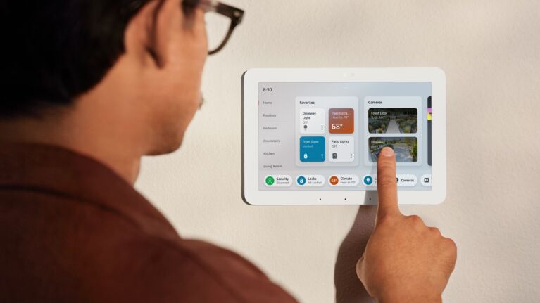 A man using a wall-mounted Amazon Echo Hub to monitor his smart cameras.