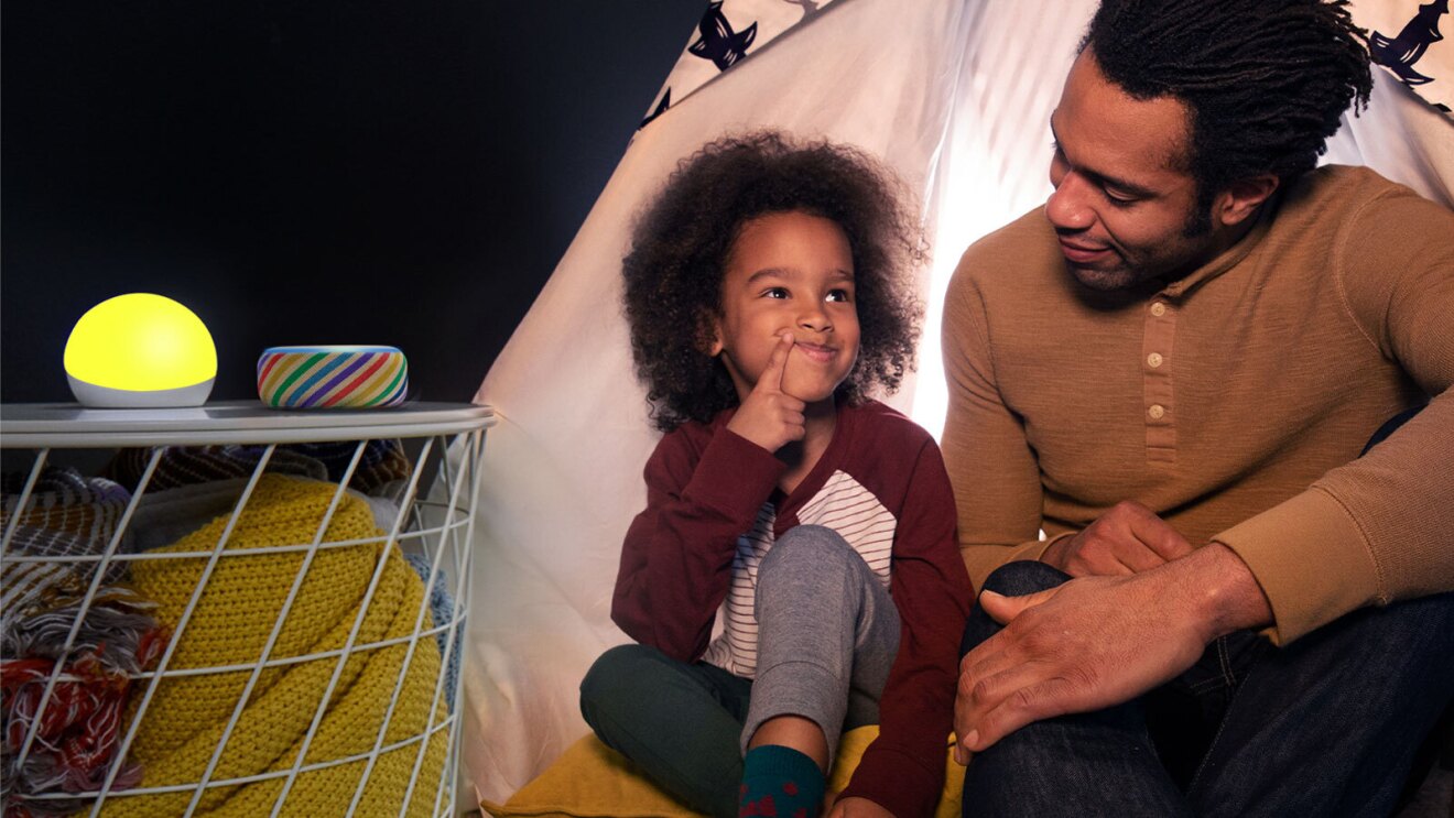 An image of a dad and son together and a side table next to them. There are two Echo Kids devices sitting on the table. 