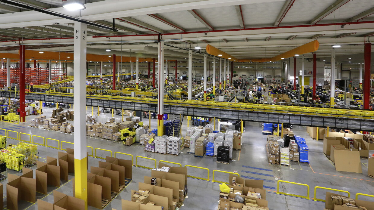Centro logísitco de Amazon en San Fernando de Henares, MAD4. La foto está tirada desde lo alto de una torre de almacenaje. Se ve una tira mecánita de color amarillo y estanterías de cartón. 
