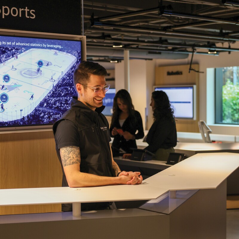 A man stands at a a counter and engages with a woman on the other side of it, inside the new AWS Skills Center in Seattle, Washington. 