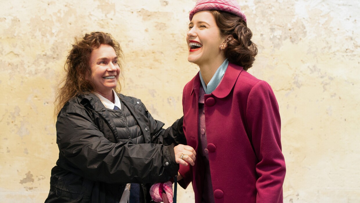 An image of a woman fixing a piece of a costume on an actress. Both are smiling and laughing.