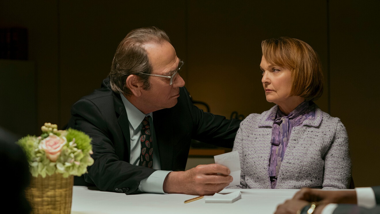 Tommy Lee Jones and Pamela Reed looking at each other while sitting at a table in the movie, The Burial.