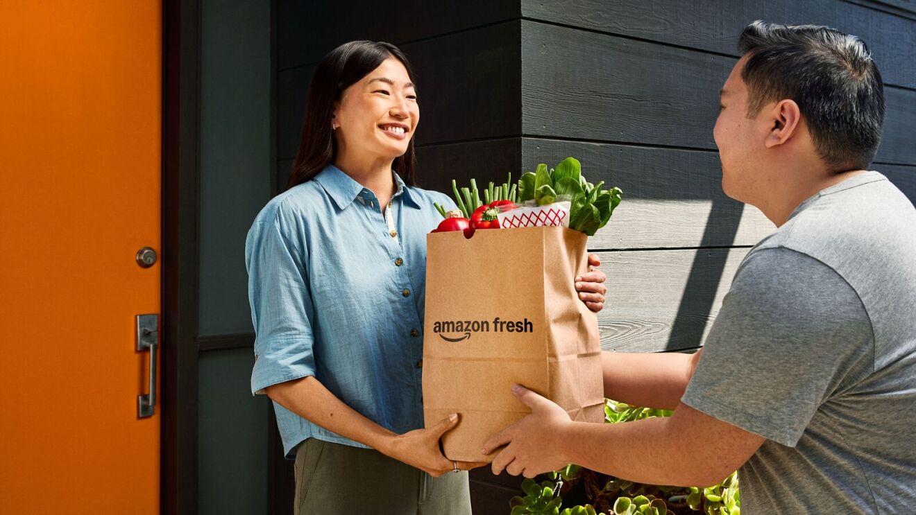 Amazon Fresh delivery person handing grocery bag to smiling customer at doorway
