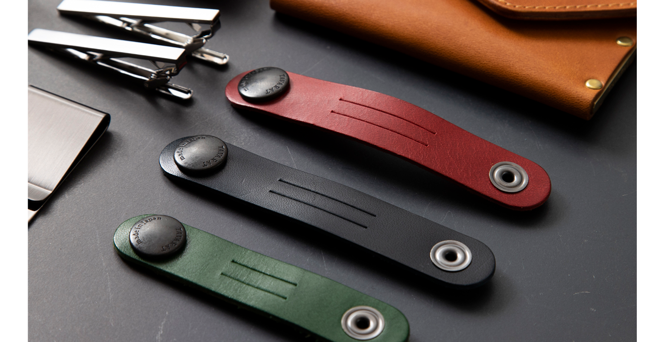 グリーン・ブラッグ・レッドのコードクリップと、ネクタイピン、マネークリップ、本革に真鍮をあわせた名刺入れなどの写真
