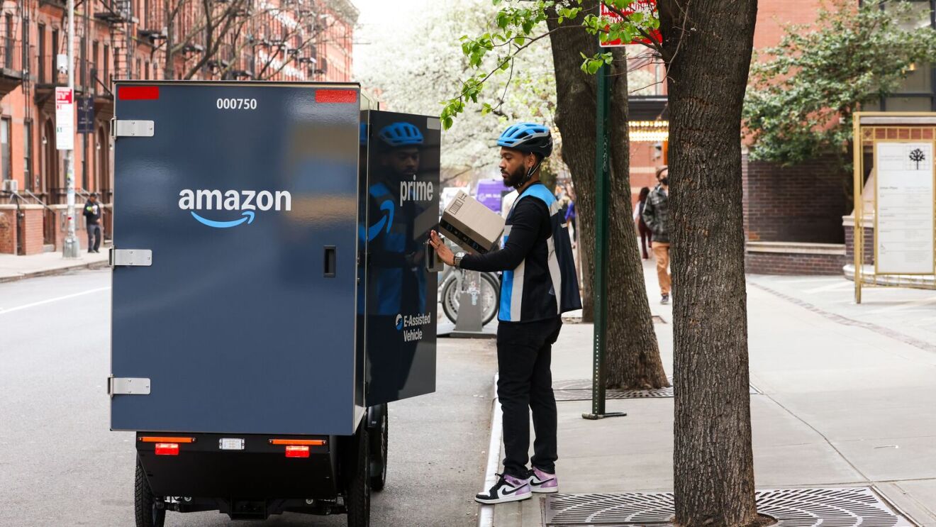 Amazon delivery person loading package in cargo compartment of e-bike on city street