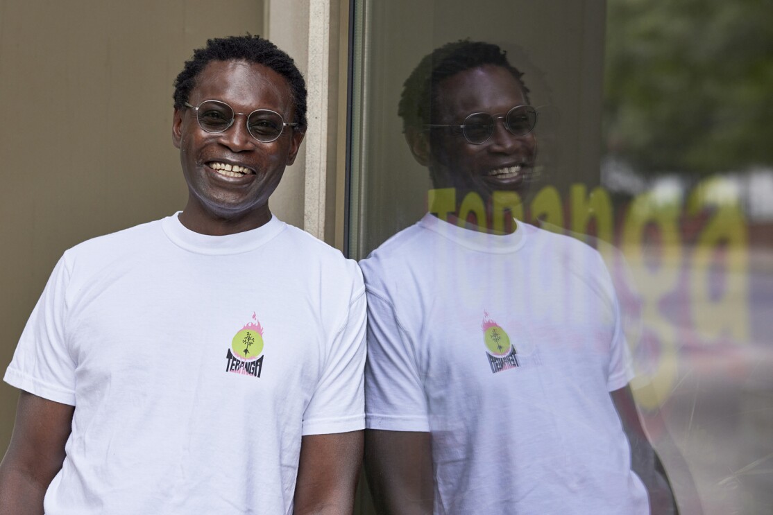 An image of a man smiling and leaning against a storefront window.