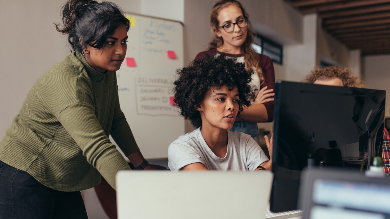 Four woman gather around a computer monitor in a classroom.