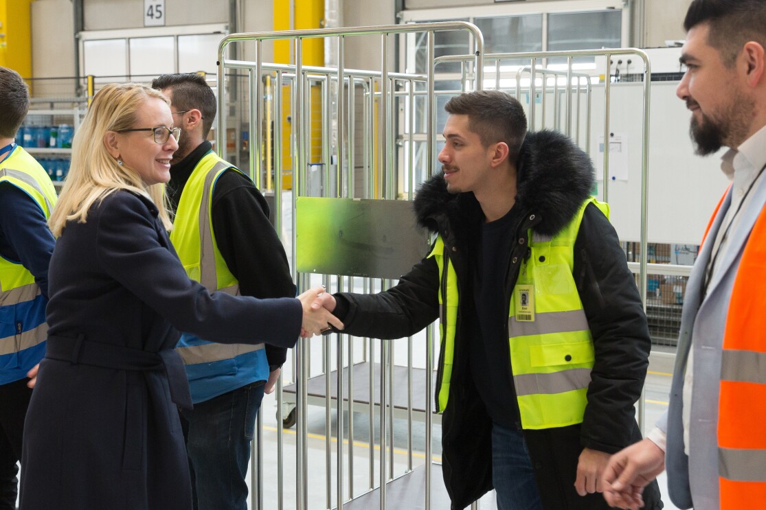 Die Wirtschaftsministerin und ein Mitarbeiter in gelber Sicherheitsweste schütteln sich die Hände. Im Hintergrund: weitere Mitarbeiter und Besucher.