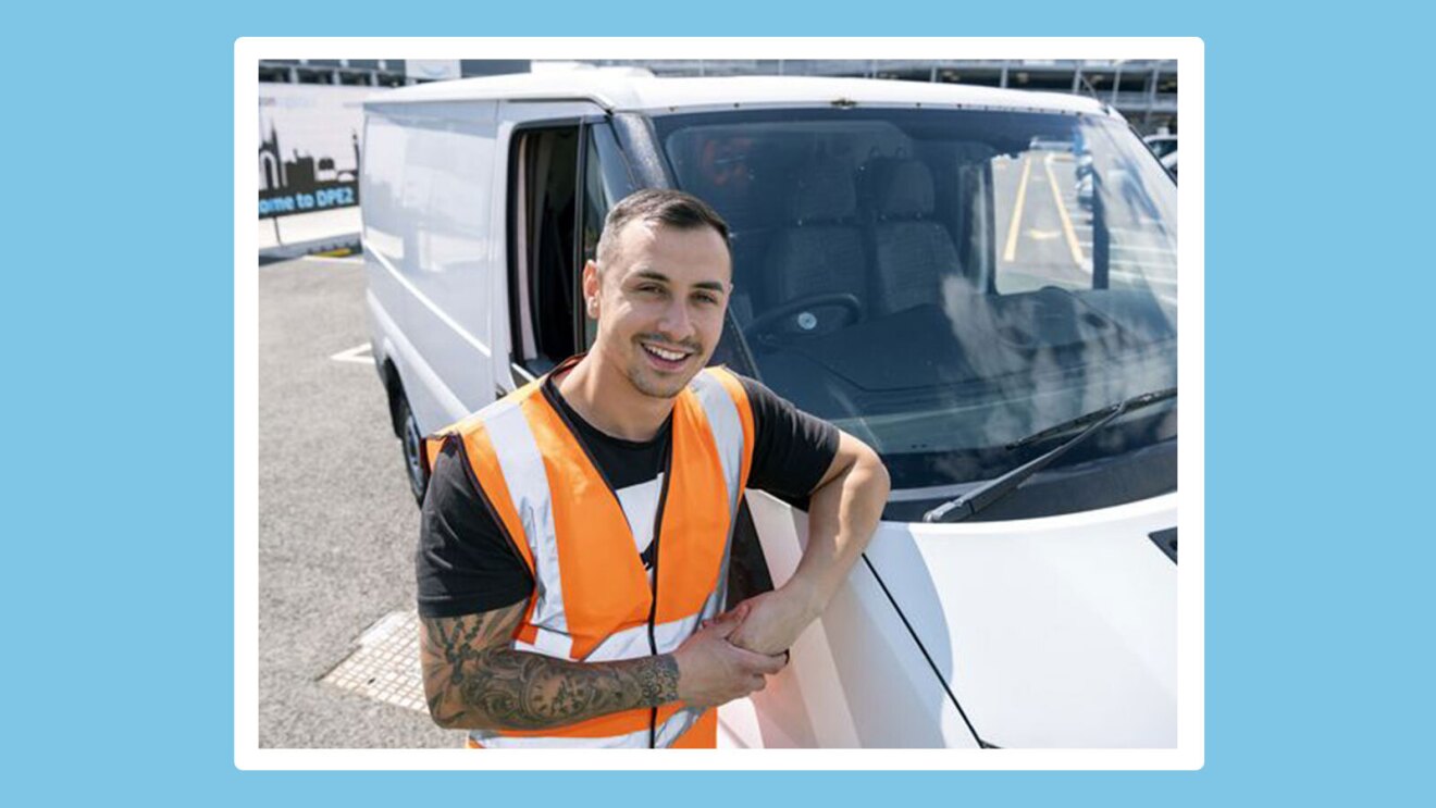 Claudiu wears an orange safety vest and rests his elbow on the hood of a white delivery vehicle.