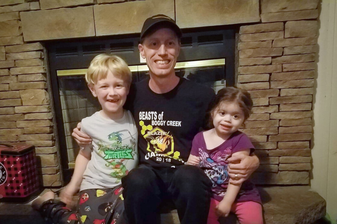 A man sits in front of a fireplace with two small kids.