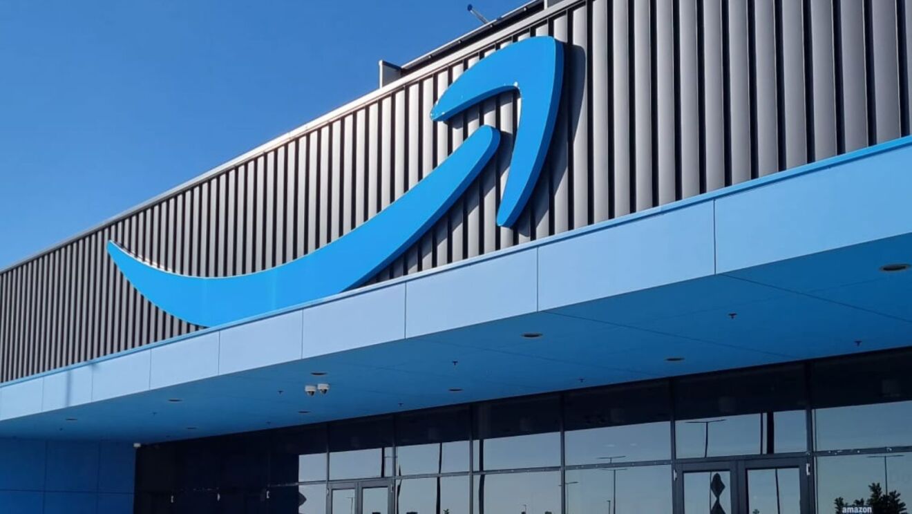 Image of the front of the BWU2 Fulfilment Centre, a large blue Amazon smile logo against blue sky.