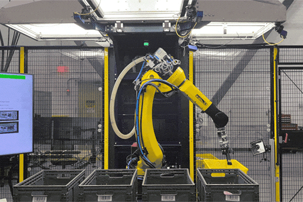 An animated GIF showing a large, yellow robotic arm picking up items from a bin and placing them in separate bins.