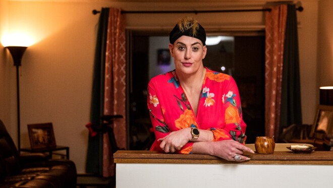 女人温柔微笑的形象照片站在她的公寓的厨房柜台。她穿着一件黑色的头巾和一个粉红色的花袍。