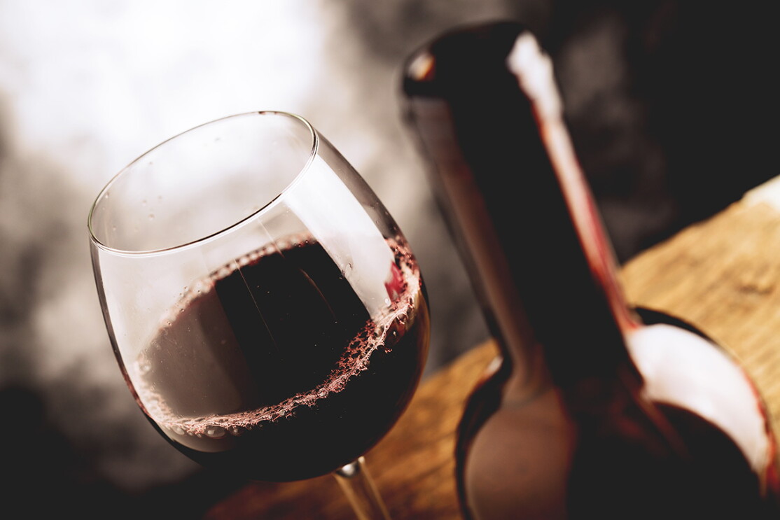 A glass of red wine and wine bottle on a rustic table. 