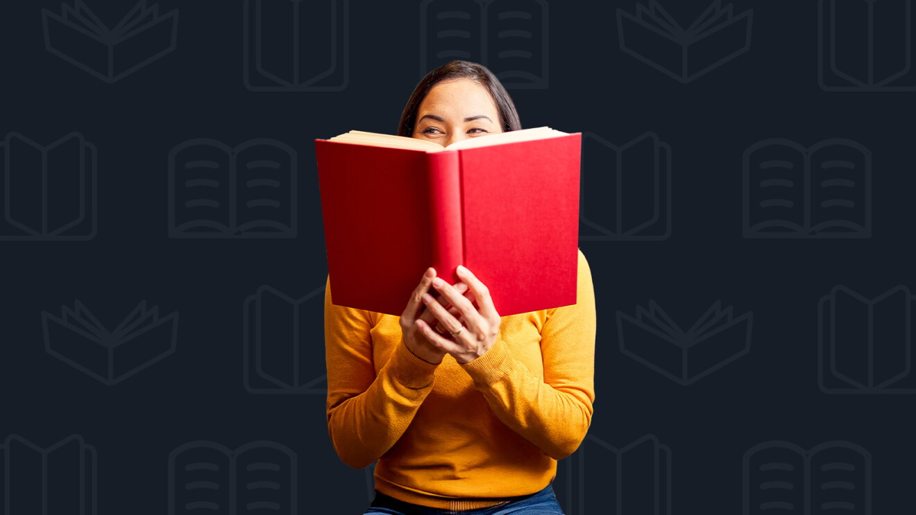 Woman wearing a yellow sweater holding a red book in front of her face, peeking over it with a playful expression. The background is dark with a pattern of faint, outlined book icons.