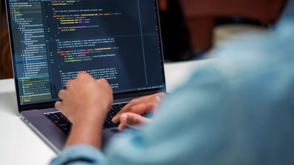 Imagen de un ordenador en el que se ve que uan silueta difuminada está programando. 