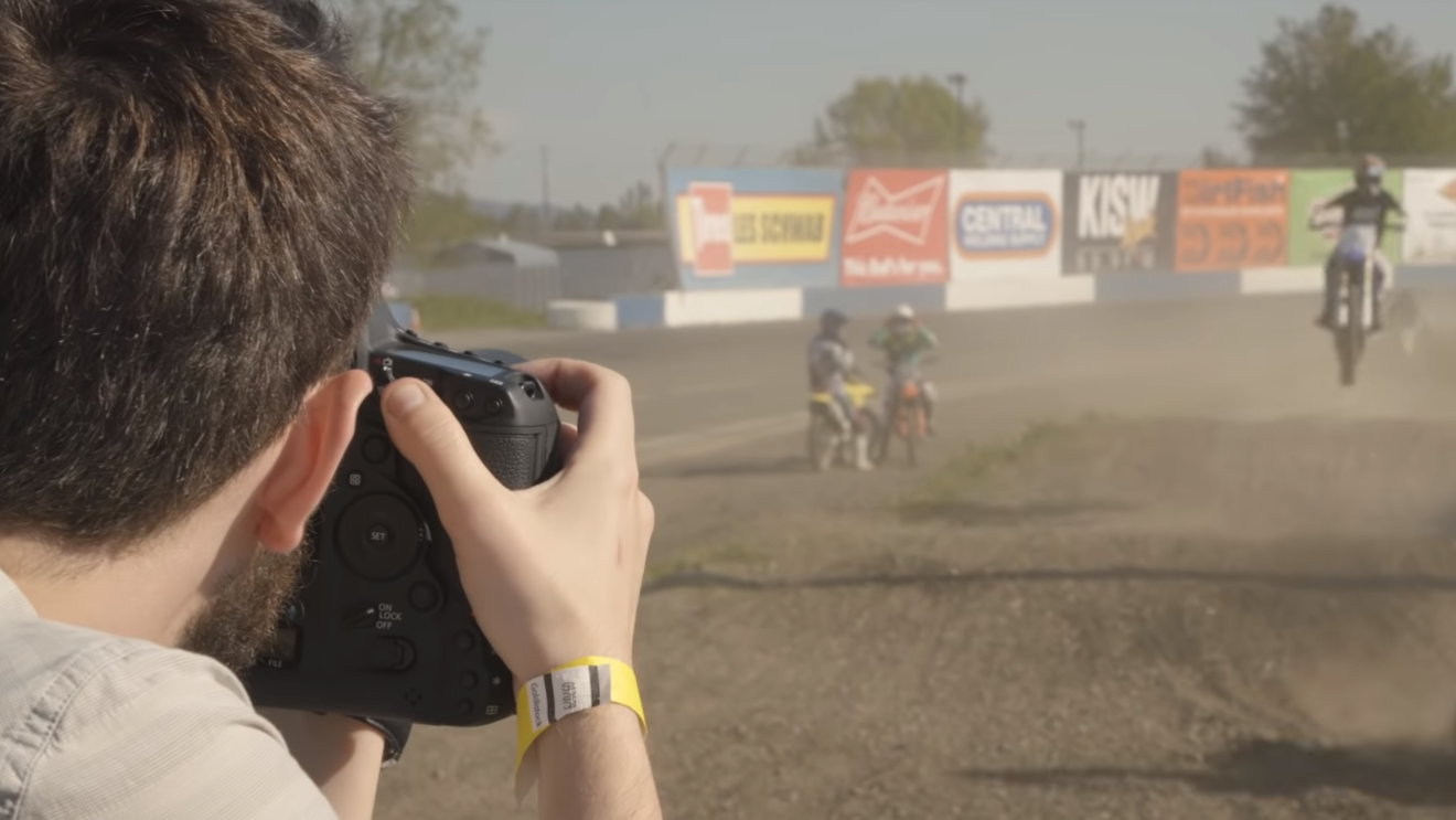 A man trains his camera lens on dirt bike racers as they zoom around the track. 