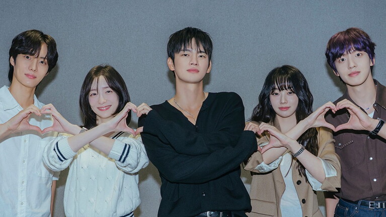 Cast members link arms and form a heart shape with their hands