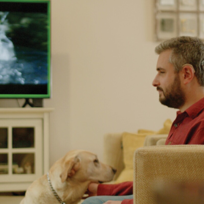 Man with a Cochlear implant watching TV with dog on couch