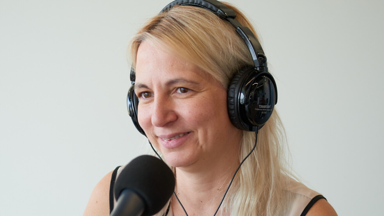 Amanda Machado, CEO de Andrés Machado, sentada en una mesa delante de un micrófono y con unos auriculares puestos. Ella está mirando al infinito. Lleva el pelo largo con pelo castaño. Con una camisa  estampada con puntos y cuadrados dibujados y pinceladas de colors como morado, verde, rosa o naranja.