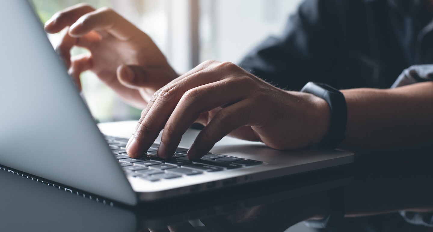 Person wearing a smart band typing on a laptop