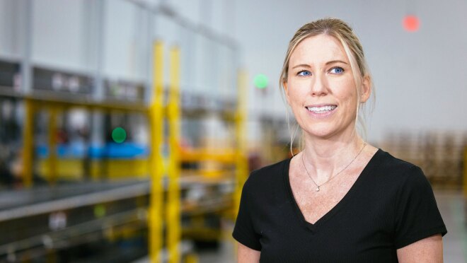 一名身穿黑色t恤的女子微笑着在亚马逊物流中心摆姿势拍照。