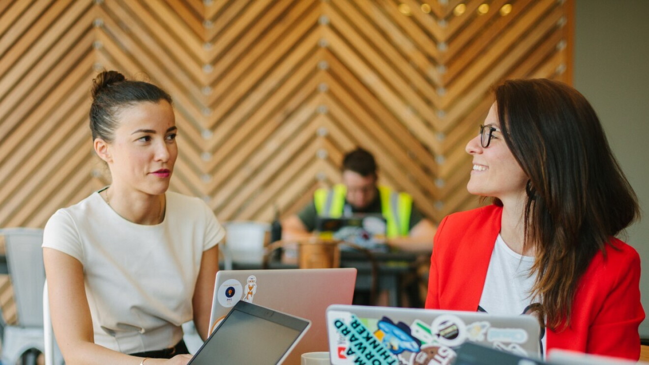 Drei Frauen sitzen am Schreibtisch, arbeiten zusammen und sprechen miteinander