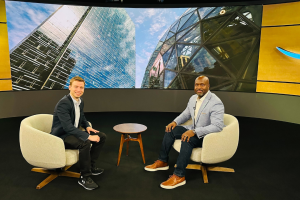 Two men smile for a photo sitting across from one another in an interview setup.