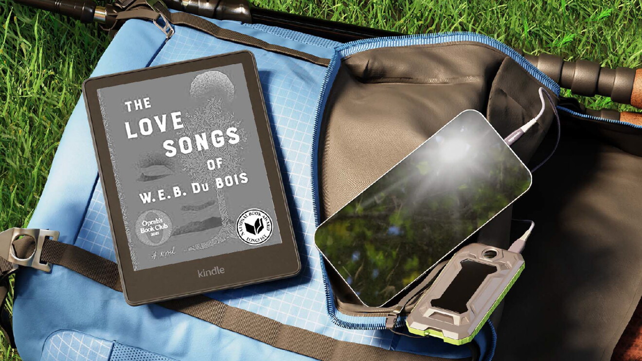 Prime Day 2023 live blog best deals: Kindle displaying "The Love Songs of W.E.B. Du Bois" while laying next to a phone resting on a backpack on grass.