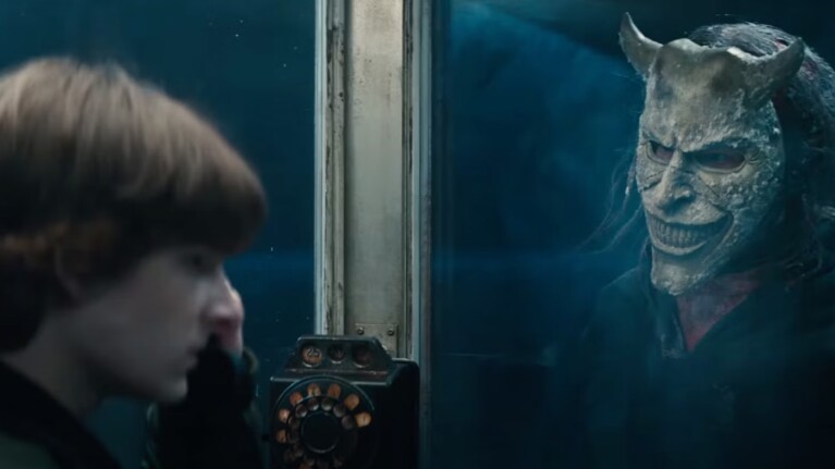 Boy on a black phone with a man in a mask next to him behind a glass wall