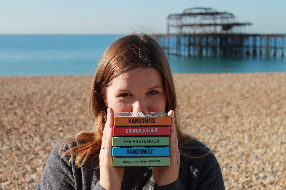Hazel Reynolds, Founder of Gamely Games, standing in a beach holding all of her games. 