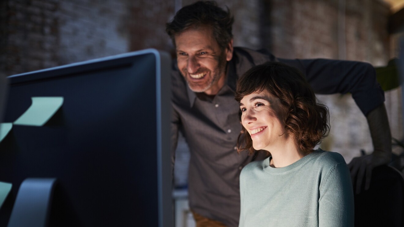 男人和女人看电脑屏幕。两个人都笑。监控灯光脸上的光在一个黑暗的屋子里。