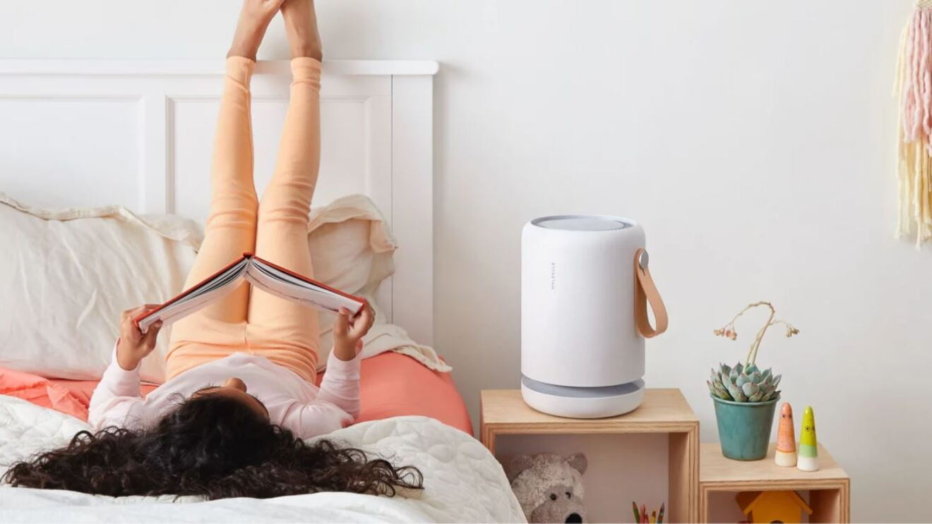 Ein Mädchen liegt auf einem Bett und ließt. Neben ihr steht eine große weiße Alexa.