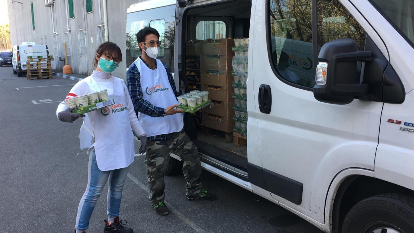 Due volontari di Banco Alimentare Lombardia davanti a un furgone con i pasti. 