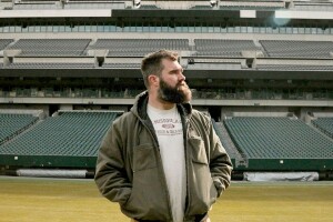 Kelce stands in the middle of a football field in an empty stadium.