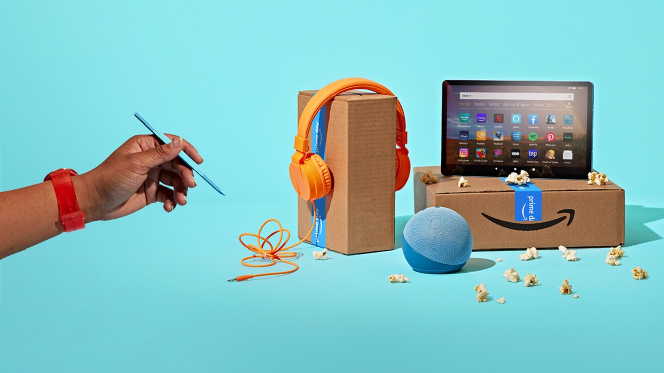 A hand holding a stylus approaches a cluster of prime shipping boxes, echo devices, headphones, and popcorn on a turquoise backdrop.