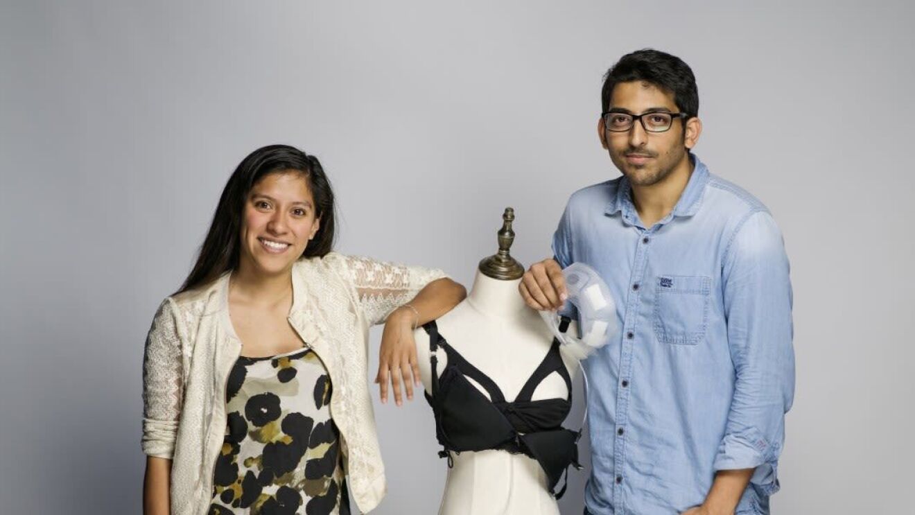An image of a man and a woman smiling for a photo. Between them is a mannequin displaying a breastfeeding bra.