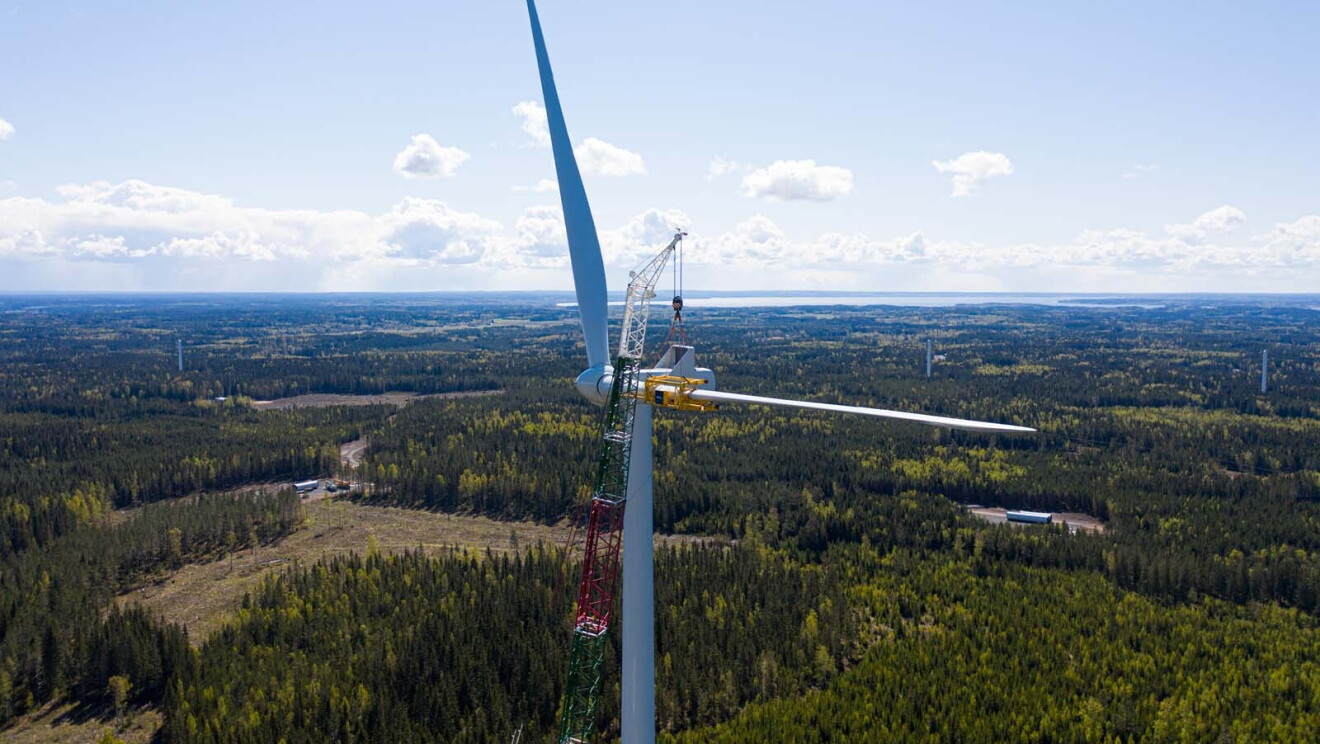 Aerial view photo of a crane assembling a wind turbine with the horizon as a backdrop, in Bäckhammar, Sweden.