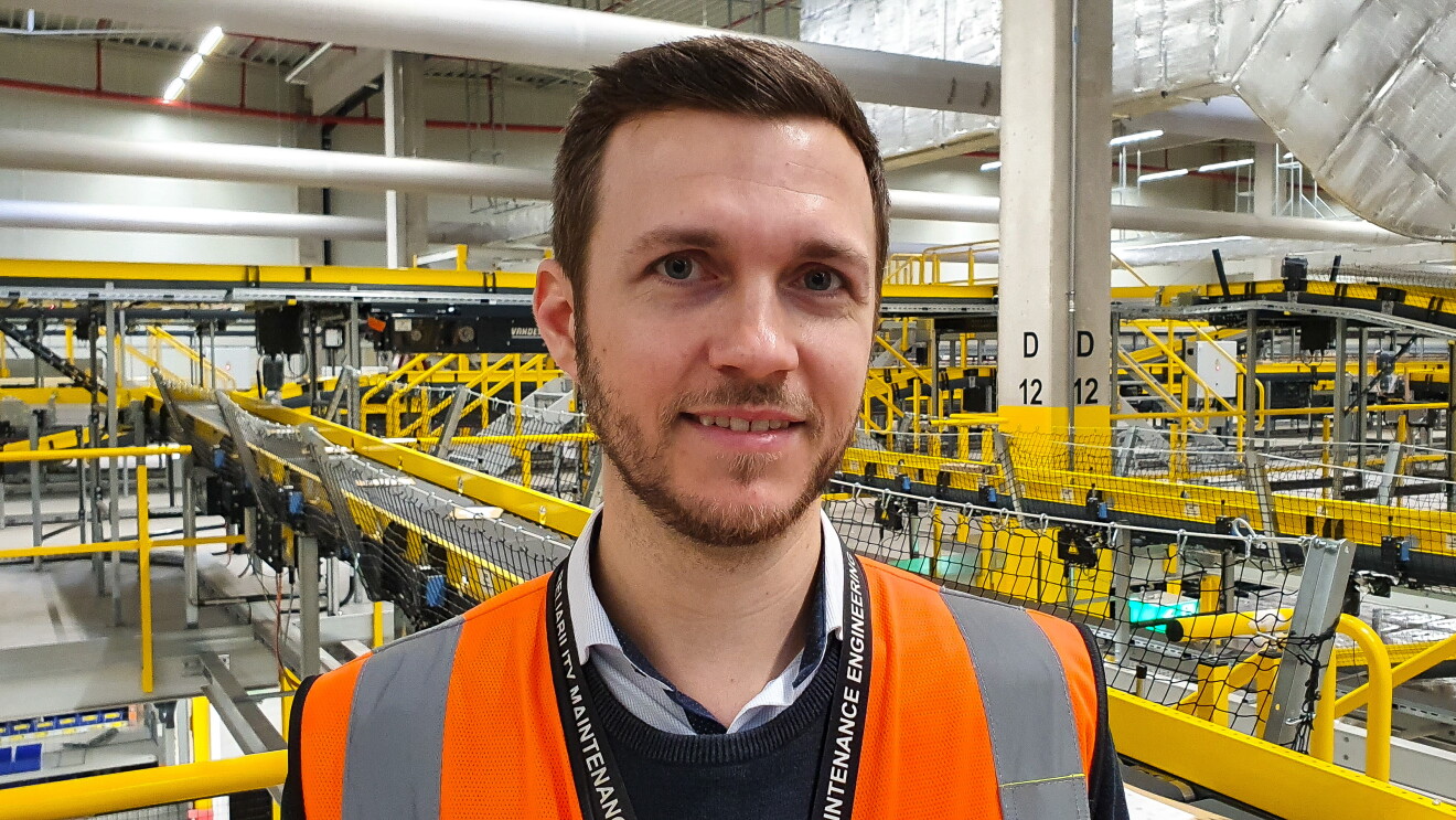 Ein junger Mann mit braunen Haaren vor einer Förderanlage im Logistikzentrum Winsen.