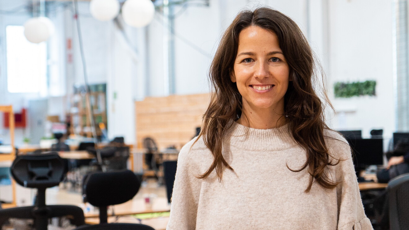 La start-up TAPP Water fue fundada por Magnus Jern y Alexander Schwarz. En la foto aparece la CEO Rocío Alcocer frente una mesa de trabajo. Rocío va un jersey también marrón muy claro. Tiene el pelo largo castaño. Mra a la cámara y sonríe. De fondo, mesas de trabajo de color madera y sillas negras.   